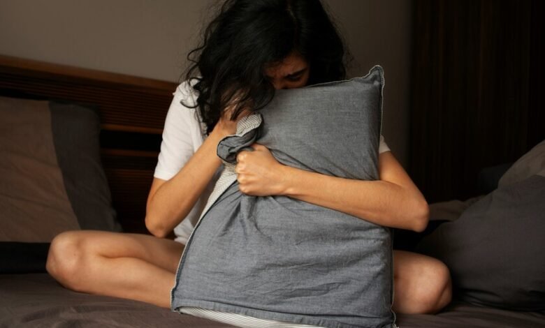 Persona acostada en la cama con la cabeza apoyada en la almohada, con una expresión de frustración y cansancio