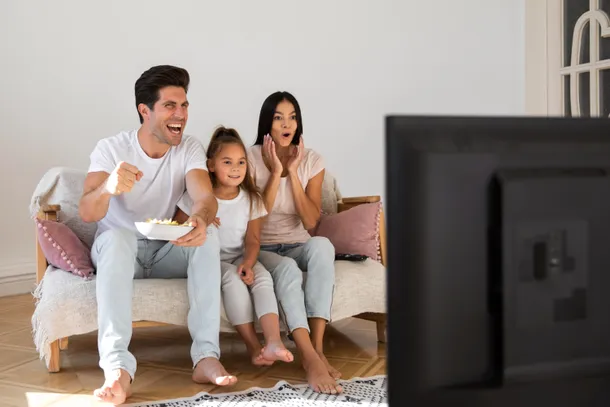 Una familia viendo TV juntos, con una pantalla de TV con varios dispositivos conectados