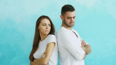 una persona sentada en una silla, con una expresión de estrés en su rostro, rodeada de personas que la están criticando