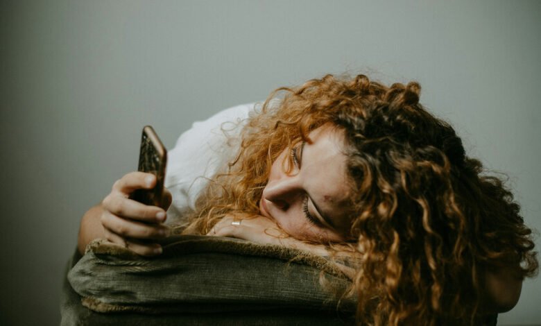 Persona sentada en un sofá, con la cabeza entre las manos, rodeada de papeles y objetos de trabajo, con una expresión de ansiedad y estrés