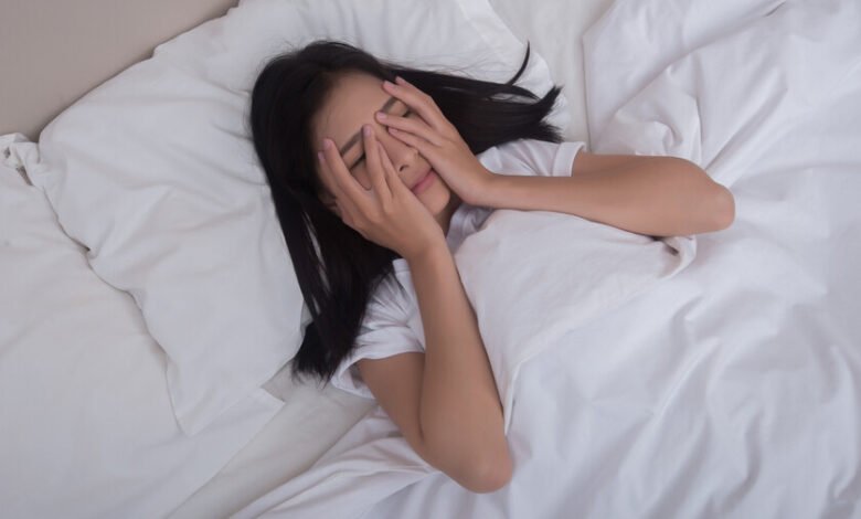 Persona acostada en la cama con los ojos cerrados, rodeada de luces suaves y un reloj en la mesita de noche.
