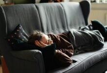 Persona durmiendo en un sofá, con un reloj en la mesa de café
