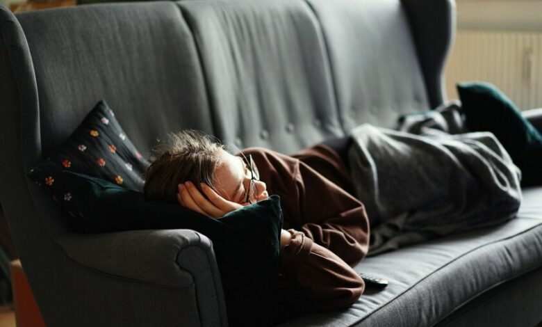 Persona durmiendo en un sofá, con un reloj en la mesa de café