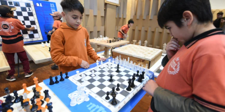 Niños jugando ajedrez en una mesa con tableros y piezas de ajedrez